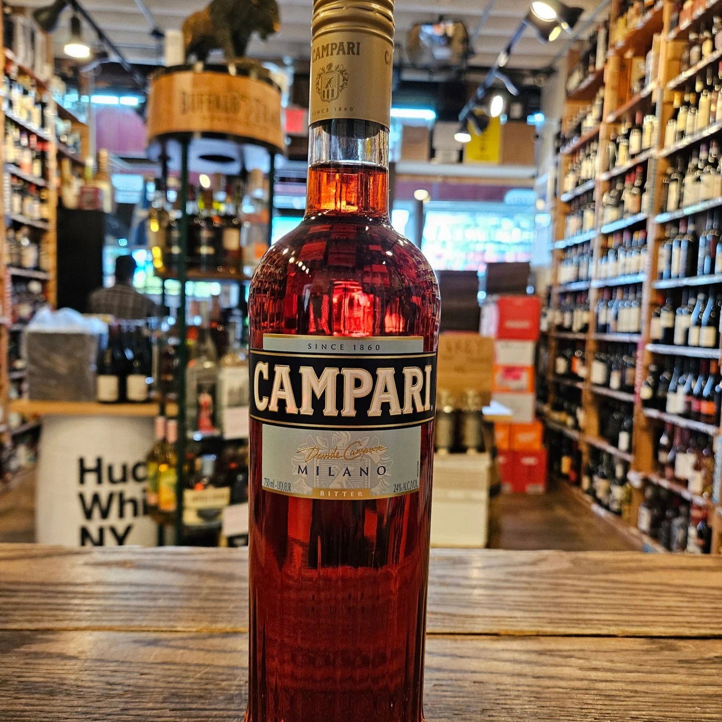 Bottle of Campari on a wooden counter with a store shelf background