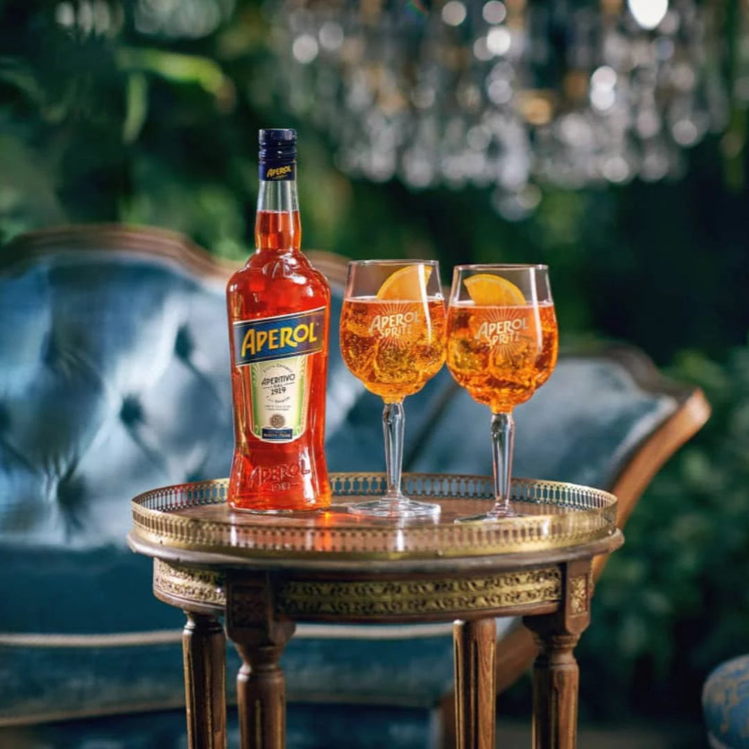 Aperol bottle with two glasses of orange cocktail on a decorative table in an elegant setting.