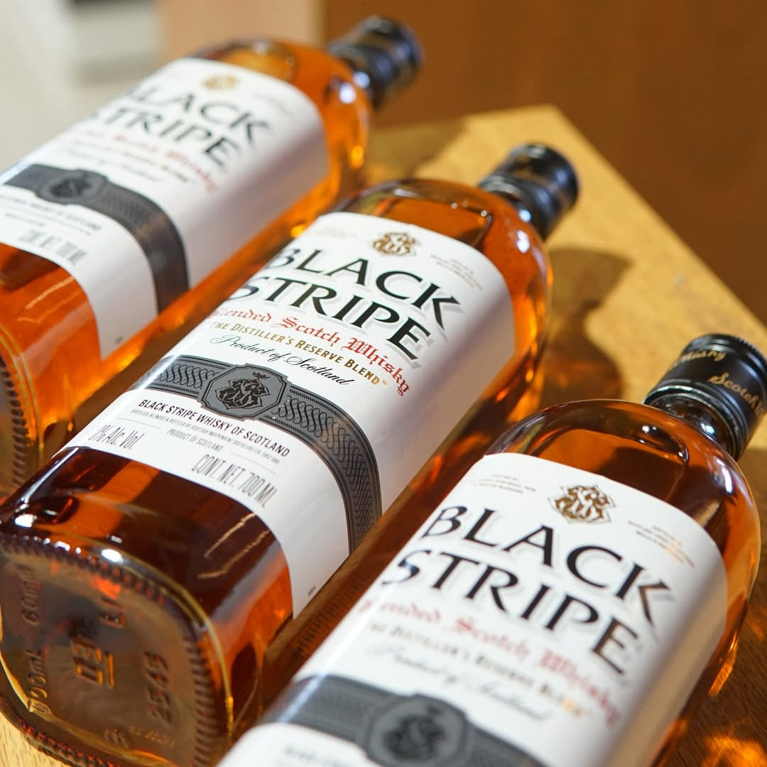 Three bottles of Black Stripe whiskey on a wooden surface with 'Licores Borda' branding.