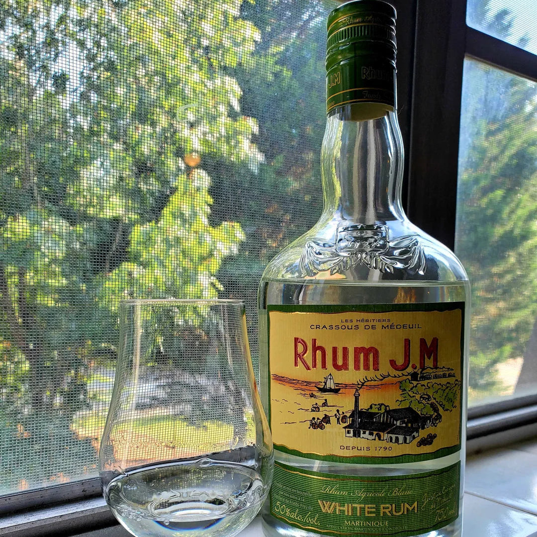Bottle of Rhum J.M. White Rum with a glass on a windowsill.