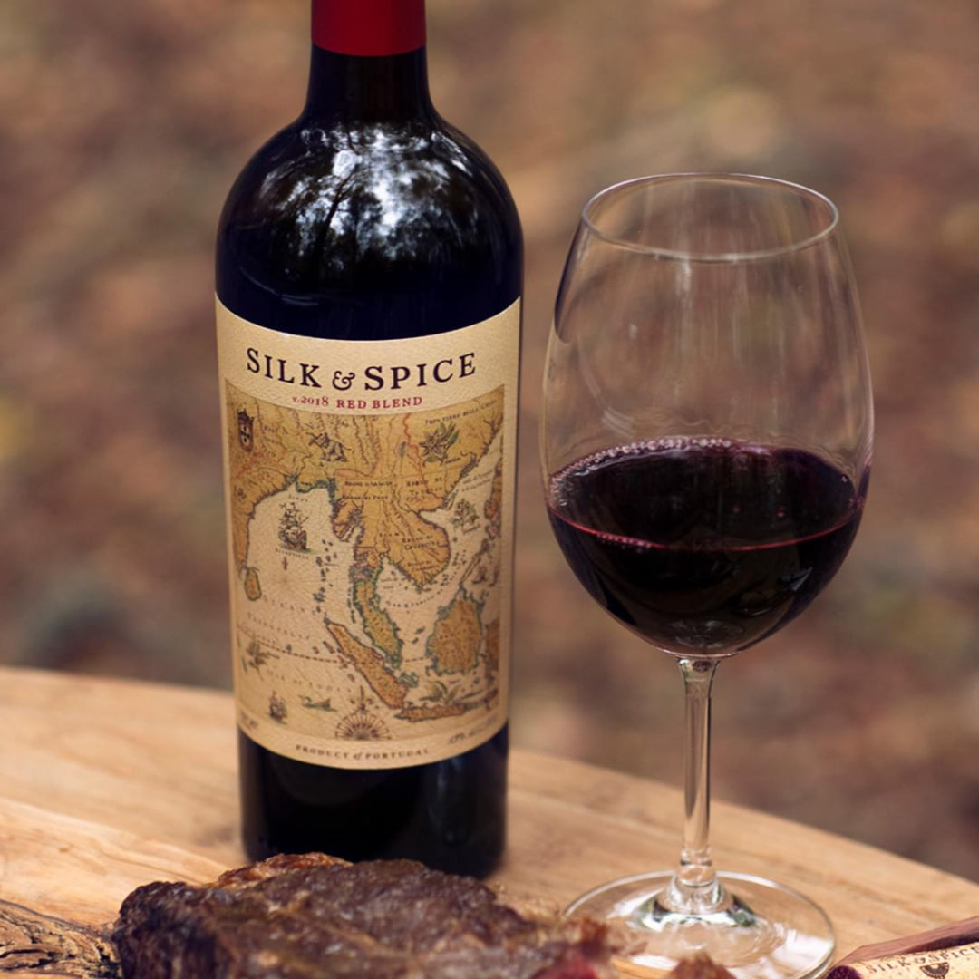 Bottle of Silk & Spice wine with a glass of red wine on a wooden surface.