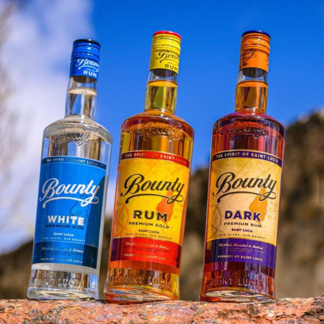 Three Bounty rum bottles in white, rum, and dark varieties on a wooden surface with a blue sky background.