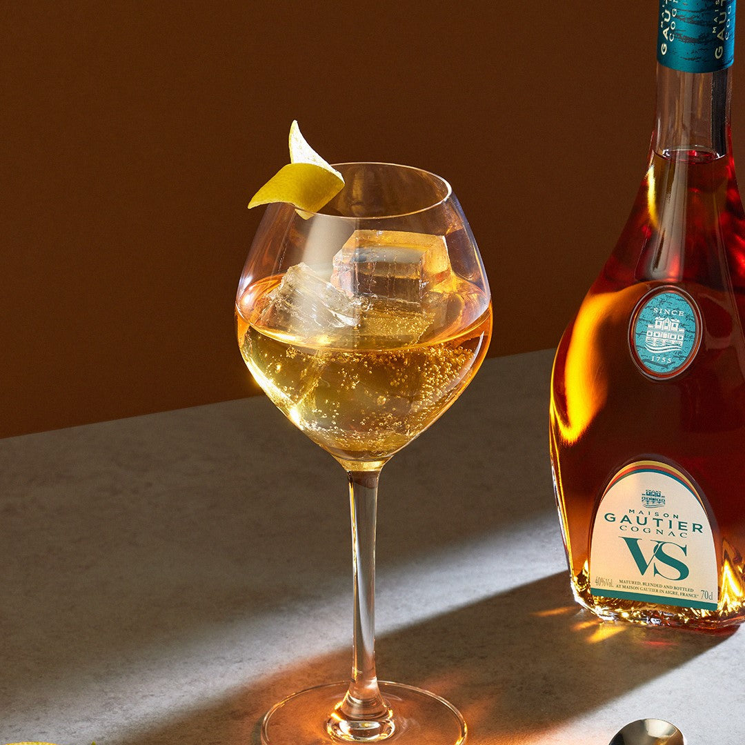 Bottle of Gautier VS cognac with a glass of white wine on a wooden surface
