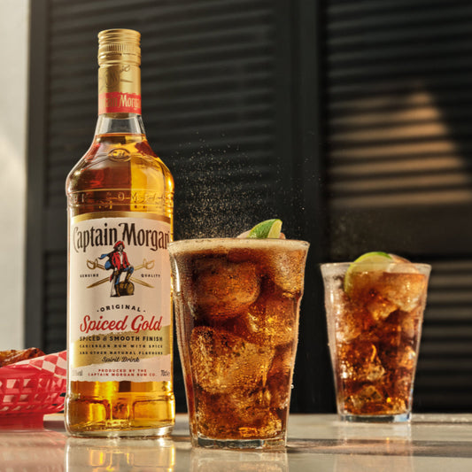Captain Morgan Spiced Gold bottle with two cocktails on a bar counter