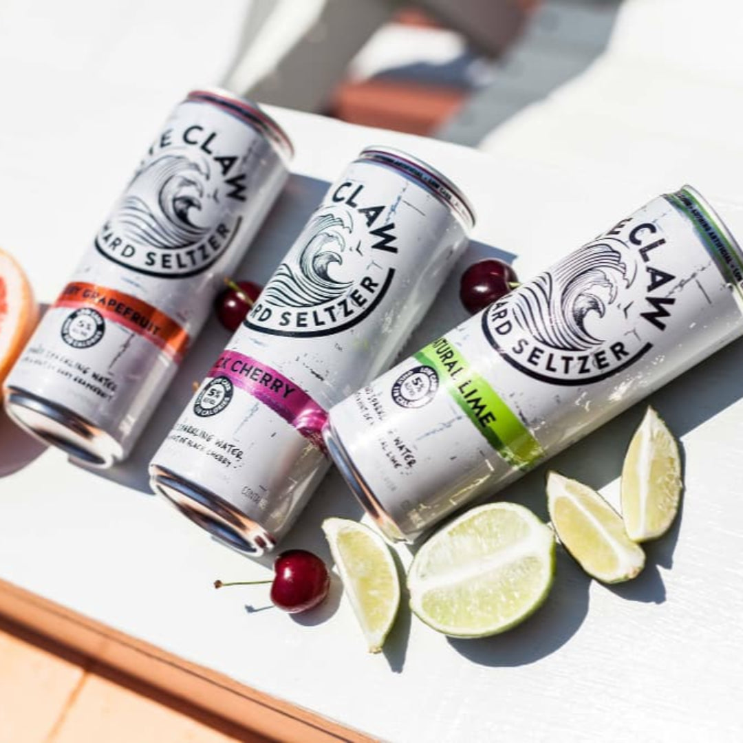 Four cans of Claw Hard Seltzer with fruit slices on a white surface