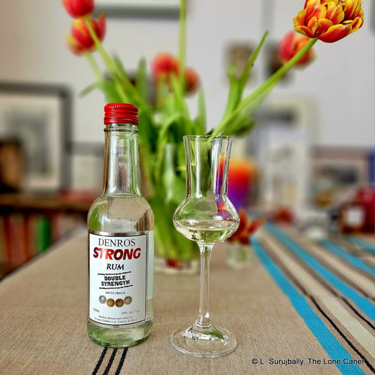 Deniro's Strong Rum bottle with a glass on a table with tulips in the background