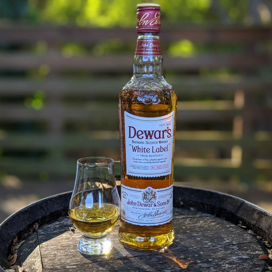 Dewar's White Label whiskey bottle with a glass on a metal tray outdoors.