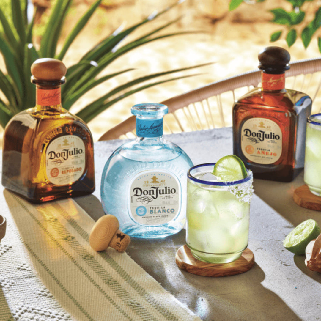 Doñ Julio tequila bottles and cocktails on a table with outdoor setting