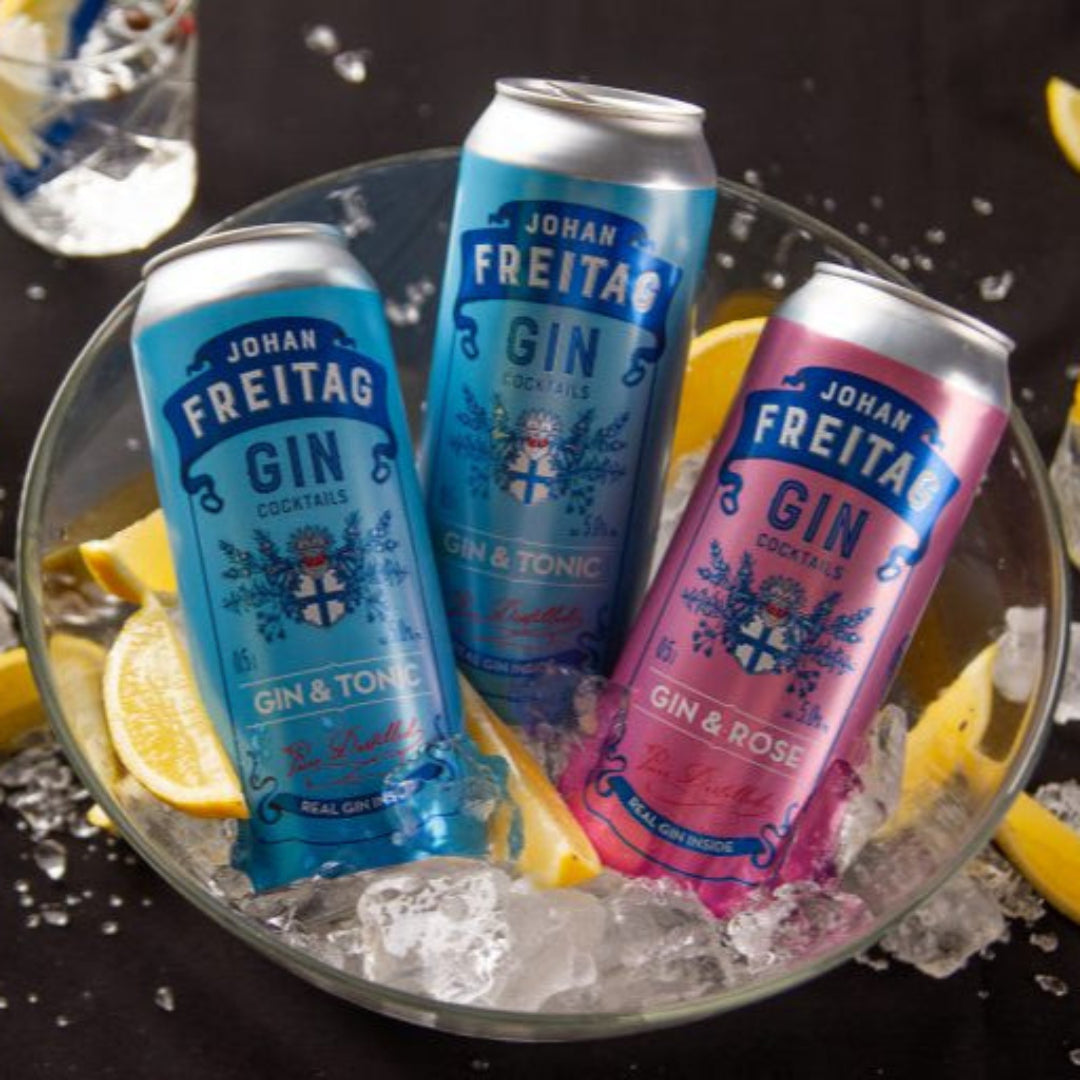 Three cans of Johan Freitag Gin on a bed of ice with lemon slices and glasses in the background.