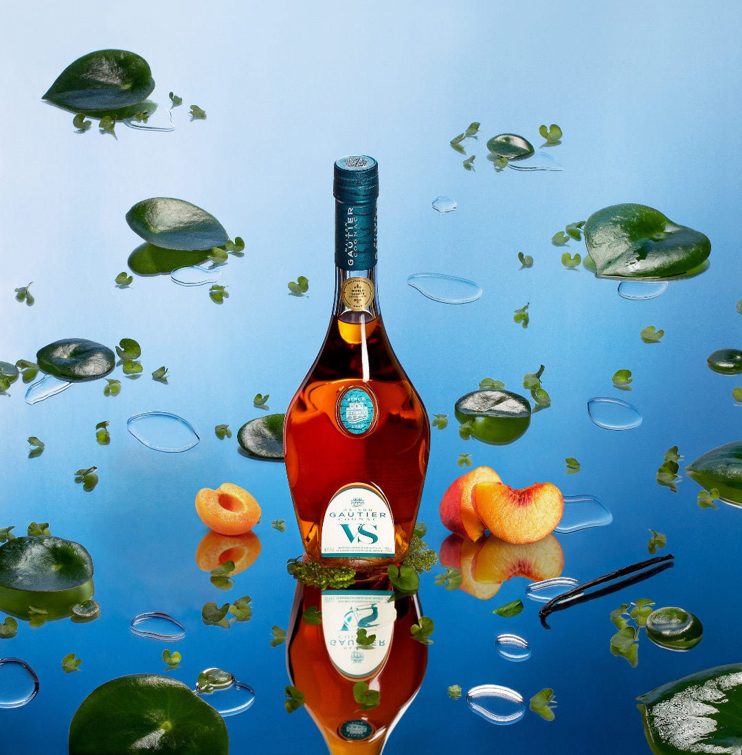 Bottle of VS cognac with peaches and leaves on a reflective water surface