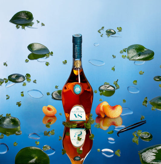 Bottle of VS cognac with peaches and leaves on a reflective water surface