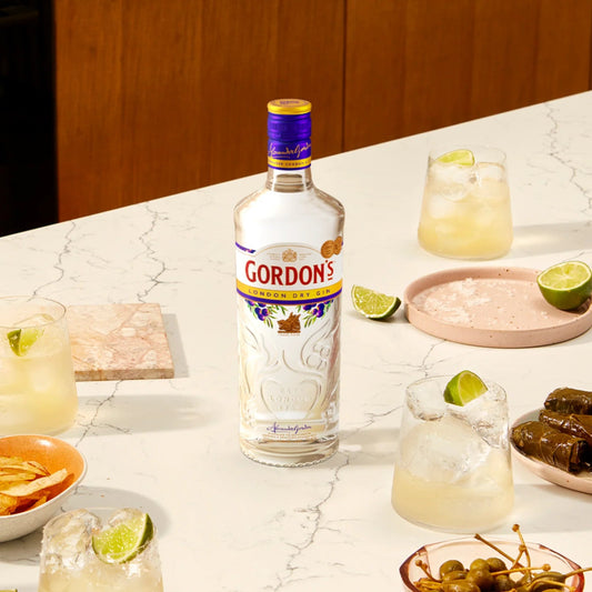 Gordon's gin bottle on a marble surface with cocktails and snacks