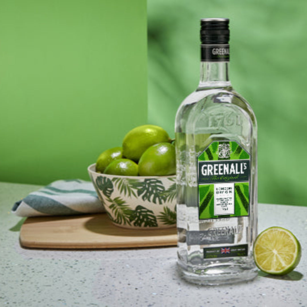 Greenall gin bottle with limes on a table against a green background