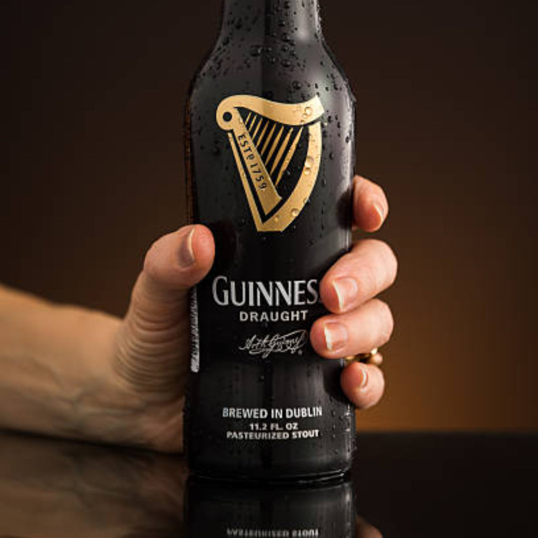 Hand holding a Guinness Draught beer bottle against a dark background