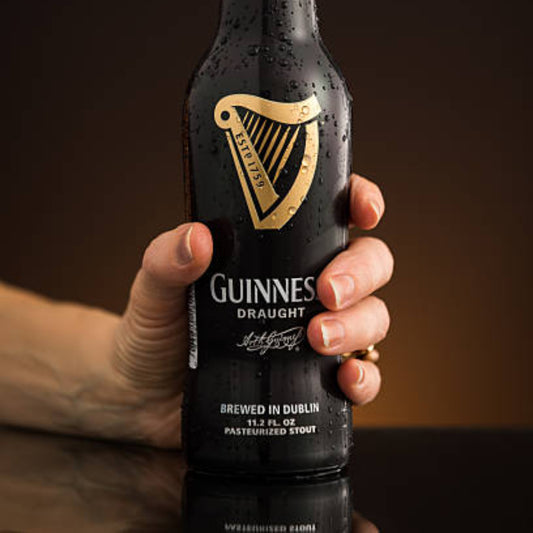 Hand holding a Guinness Draught beer bottle against a dark background