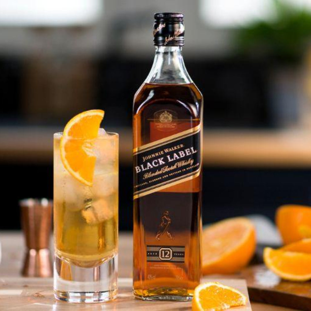 Johnnie Walker Black Label whisky bottle with a cocktail and oranges on a wooden table.