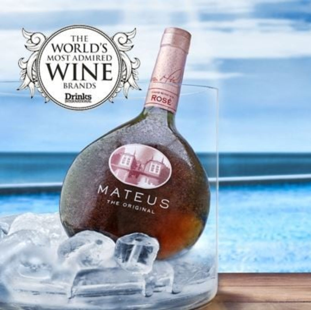 Mateus Rosé wine bottle with two glasses of wine by the ocean