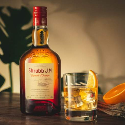 Shrubbs J.M. bottle with a glass of cocktail and oranges on a wooden surface.