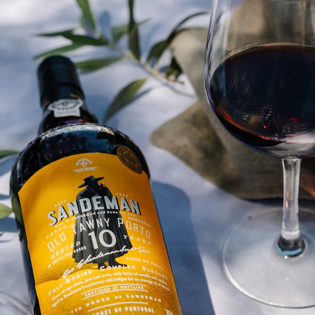 Sandeman Port bottle with a glass of red wine on a reflective surface