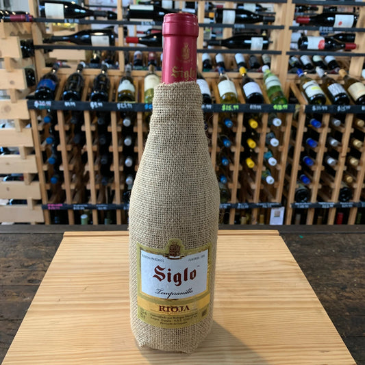 Wine bottle with jute wrap on a wooden table with a wine rack in the background