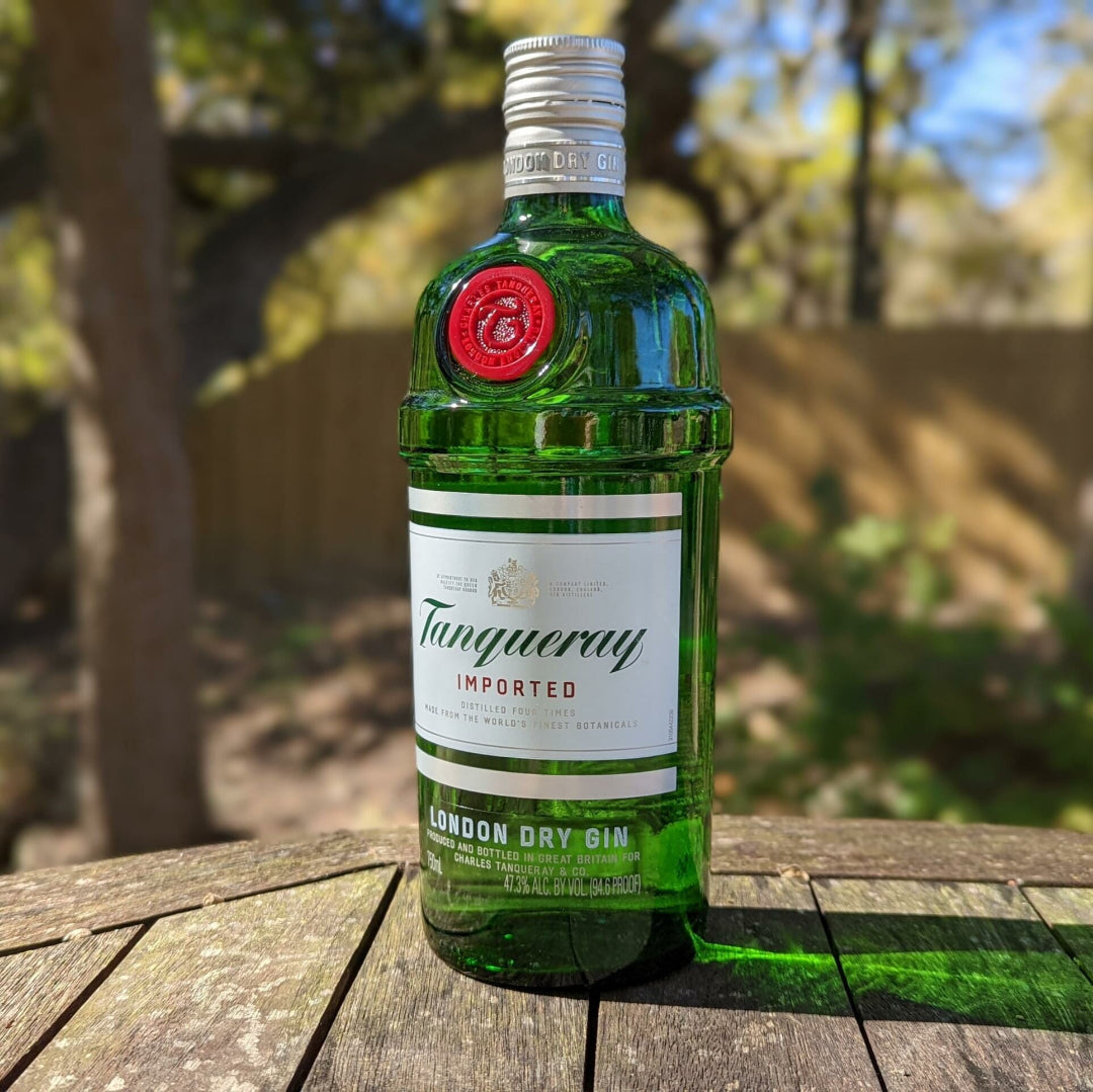 Tanqueray gin bottle on a wooden surface with a blurred outdoor background