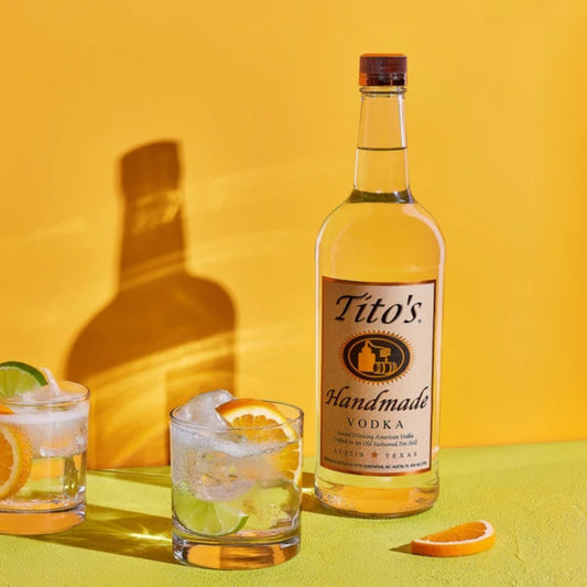 Tito's Handmade Vodka bottle with two glasses of cocktails on a yellow background