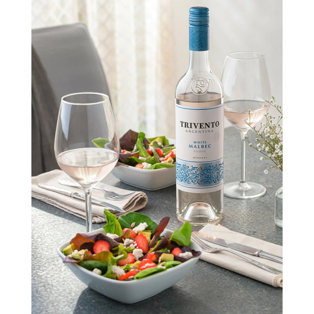 Trivento Argentine white wine bottle with two glasses and a salad on a table.