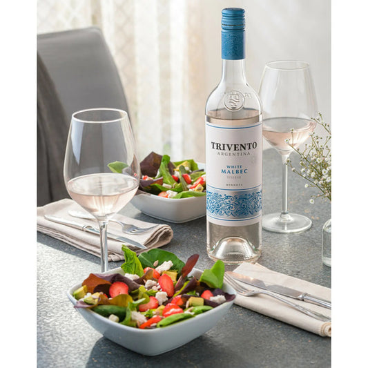 Trivento Argentine white wine bottle with two glasses and a salad on a table.