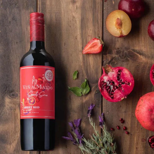 Bottle of Vina Malpo Sweet Red wine on a wooden surface with pomegranates and plums.