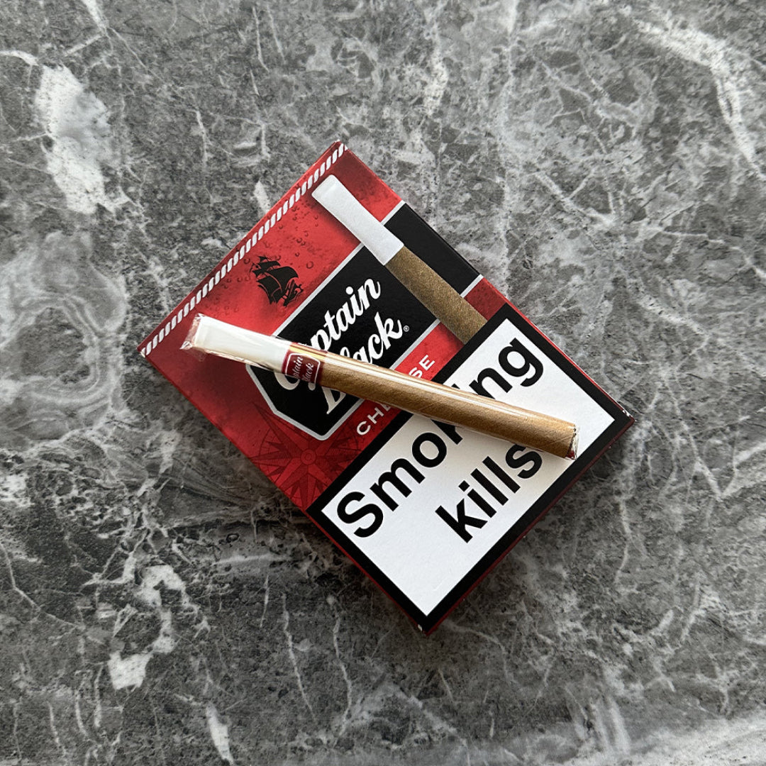 Red and white cigarette pack with a lit cigarette on a gray marble surface