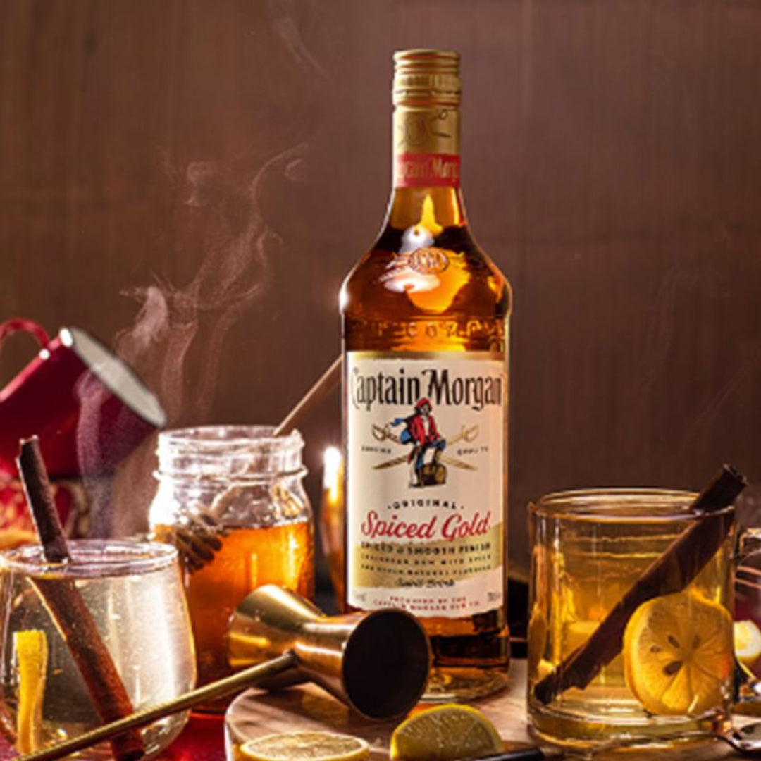 Captain Morgan Spiced Gold bottle with cocktail glasses and ingredients on a dark background