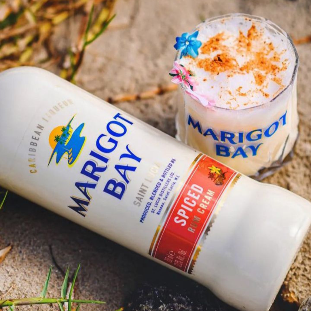 Marigot Bay spiced rum bottle and cocktail on a sandy surface with grass.