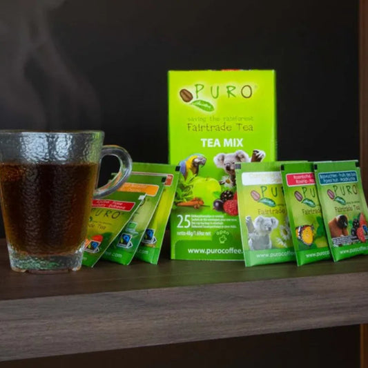 Puro tea mix packages with a steaming cup of tea on a wooden surface.