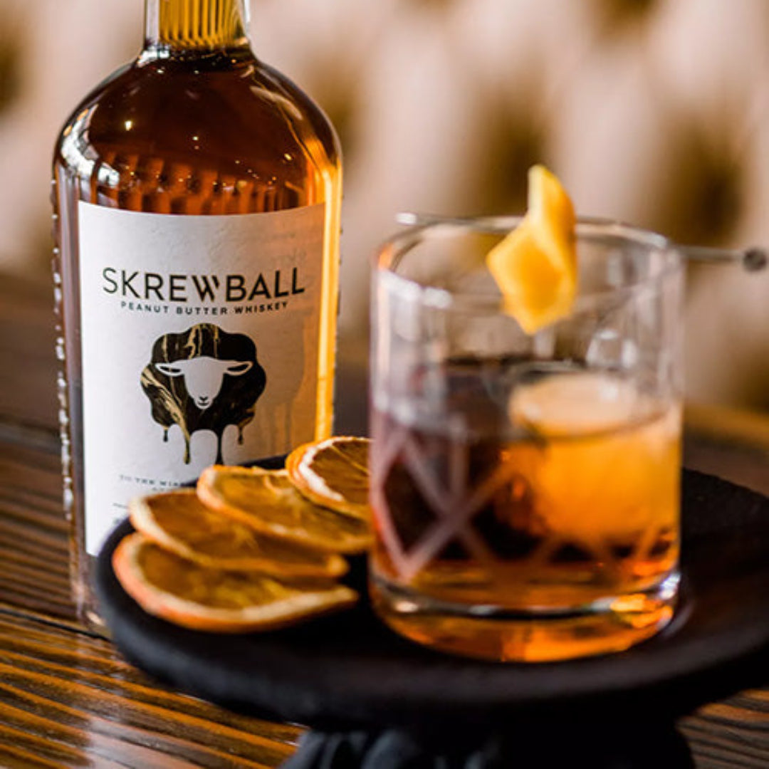 Skrewball whiskey bottle with a glass of whiskey and orange slices on a wooden table.